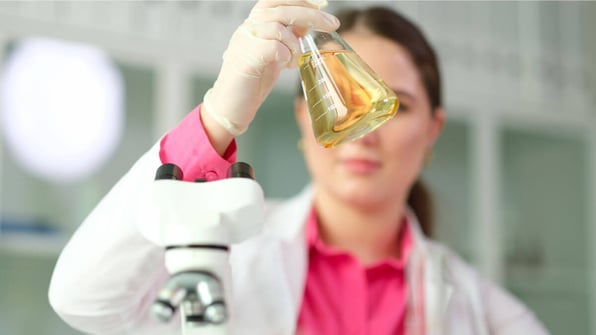 Female scientist looking at a triangular flask filled with yellow liquid | Scilife