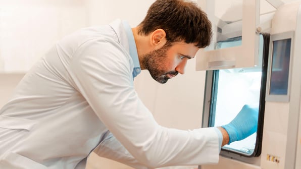 Lab technician in a white coat closely inspecting or calibrating equipment inside a laboratory-grade freezer or incubator | Scilife