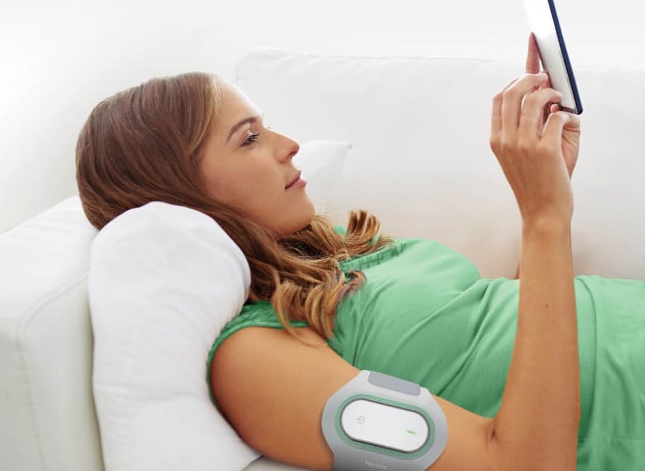 Young woman laying on a coach wearing a Nerivio Migra Device and controlling it with an iPad | QualityKick