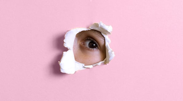 Young boy with Brown eye looking through a hole in a pink wall.