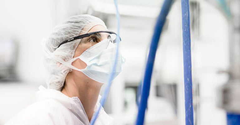 3p Bio researcher with goggles, mask and cap looking at biological research equipment.