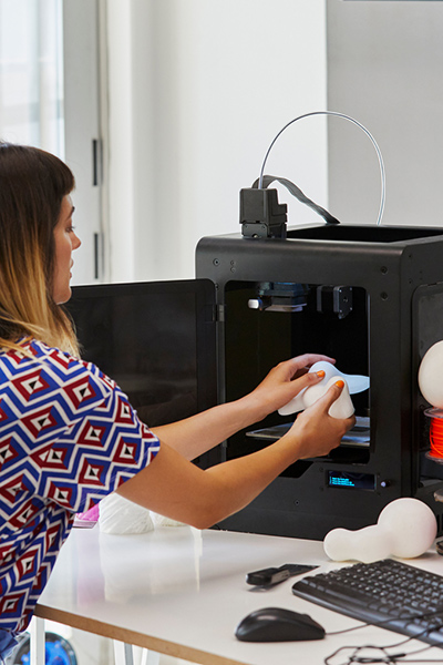 Picture of a woman working on a 3D printer with a prototype of a medical device